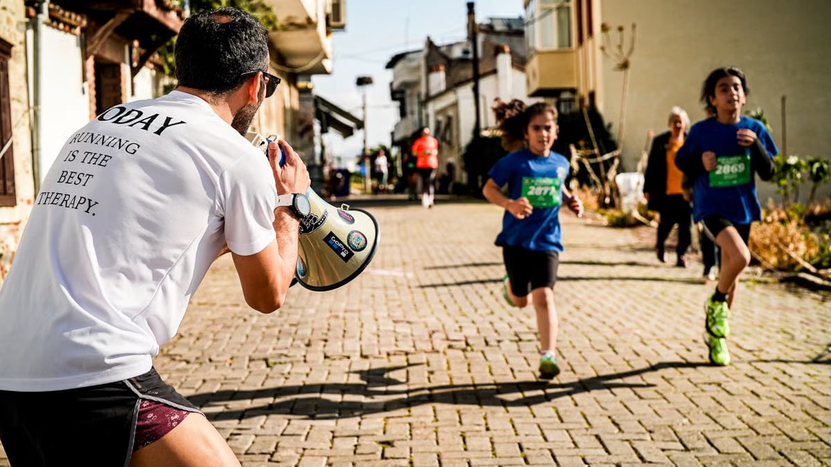 Children running a street race while a man with a megaphone cheers them on.